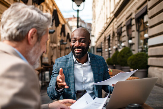 Two businessmen discussing documents at outdoor city cafe