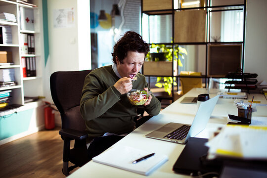 Man eating salad at desk in modern office