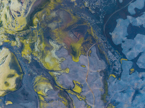 Aerial view of the rugged Icelandic Highlands featuring vibrant green mossy lava fields, dark volcanic soil, and a winding dirt road cutting through the desolate landscape, Iceland.