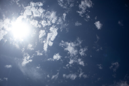 Inquadratura dal basso del sole splendente nel cielo blu parzialmente coperto da nuvole bianche e leggere sparse