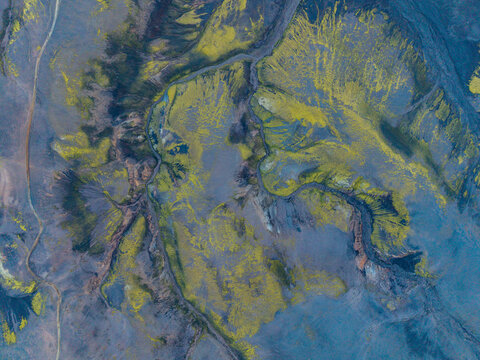 Aerial view of moss-covered volcanic terrain with dark lava rock and a winding stream in Iceland.