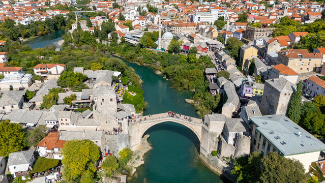 Aerial view of the Old Bridge Mostar spanning the emerald Neretva River, surrounded by stone buildings and terracotta rooftops in Mostar, Bosnia and Herzegovina.