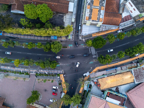 Aerial view of a busy road intersection with vehicles, lush green trees, and surrounding urban buildings in Klaten, Central Java, Indonesia.
