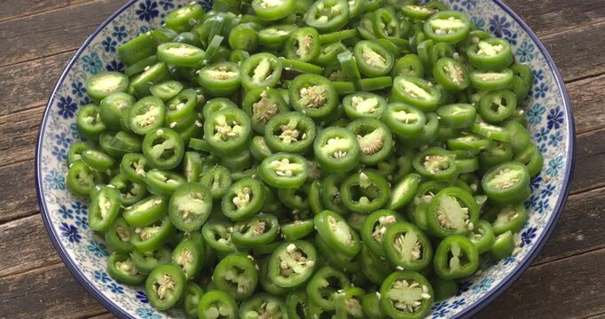 A pile of sliced, freshly harvested, unripe jalape&ntilde;o on a plate. Preparing pickled jalape&ntilde;o. Rustic wooden background, natural light, table spin.