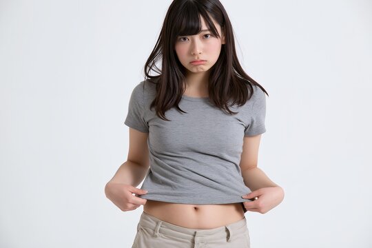 体型を気にして不満げな表情でお腹を見せる若い日本人女性