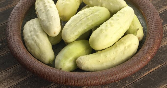 A handmade clay plate full of ripe white cucumbers (White Wonder, an old American variety) on a rustic wooden background. Table spin, natural light, 4K DCI.