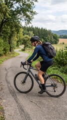 Fototapeta premium Woman cycling on a winding rural road with a backpack on a sunny day