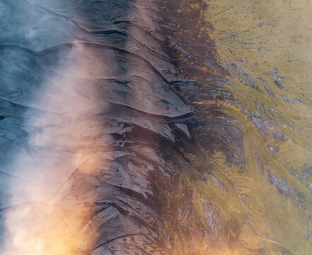 Aerial view of volcanic landscape with dark lava fields and mossy terrain partially obscured by mist in Iceland.