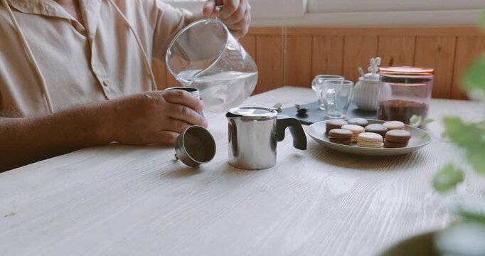 Man making coffee at home, pouring water into the bottom tank of moka pot. Preparation home coffee, morning ritual, coffee brewing process.