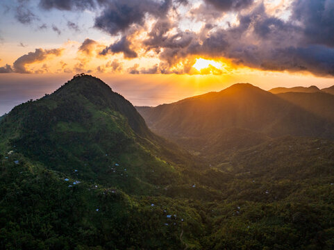 Aerial view of Lahangan Sweet featuring lush green mountain slopes, dramatic sunset clouds, and golden sun rays illuminating the valley in Kecamatan Abang, Bali, Indonesia.