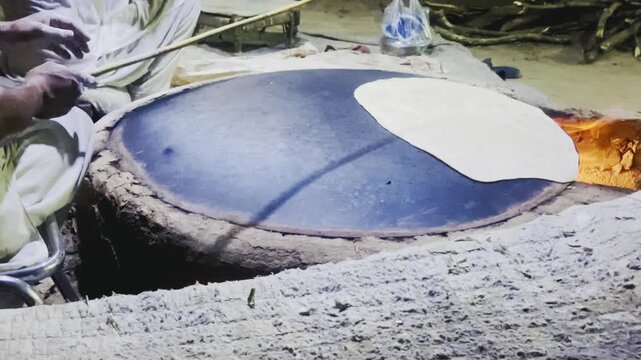 Traditional baker cooking flatbread rumali roti on large convex iron tawa plate