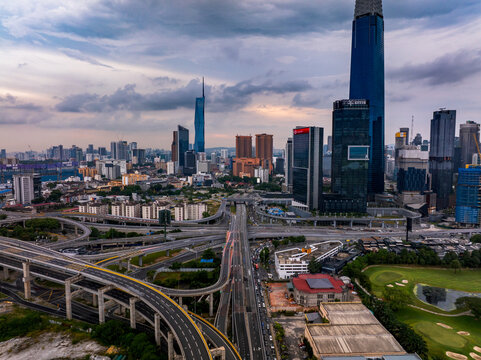 Aerial view of the modern skyline featuring skyscrapers, complex highway interchanges, and urban infrastructure under a cloudy sky in Kuala Lumpur, Federal Territory of, Malaysia.