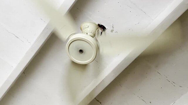 Electric ceiling fan spinning at high speed on a white wooden ceiling