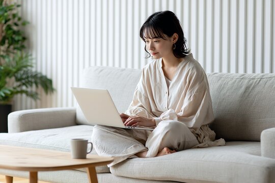 ソファでノートPCを操作する若い日本人女性の在宅ワーク風景