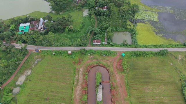 Overhead top-down drone shot showing a uniquely shaped oval dirt track or ground pattern surrounded by green paddy fields and countryside.
