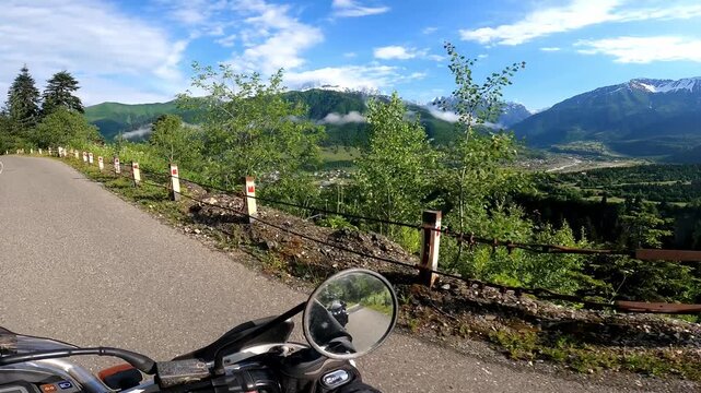 POV motorcycle ride along a mountain road passing a breathtaking panoramic viewpoint over Mestia, Svaneti, Georgia. Scenic travel footage with alpine landscape and mountain village views