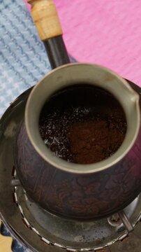 Ground coffee sits inside a vintage metal cezve pot placed on a portable burner outdoors. Concept of traditional brewing, wilderness culinary craft, authentic coffee making, and morning routine.