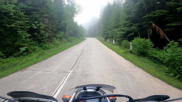 POV motorcycle ride along a foggy mountain road through evergreen forest in Svaneti, Georgia. Atmospheric adventure journey with scenic views, winding asphalt road and immersive riding experience
