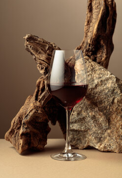 Glass of red wine with old driftwood and a piece of granite rock on a beige background.