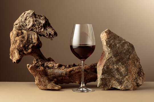 Glass of red wine with old driftwood and a piece of granite rock on a beige background.