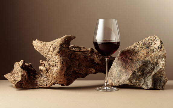 Glass of red wine with old driftwood and a piece of granite rock on a beige background.