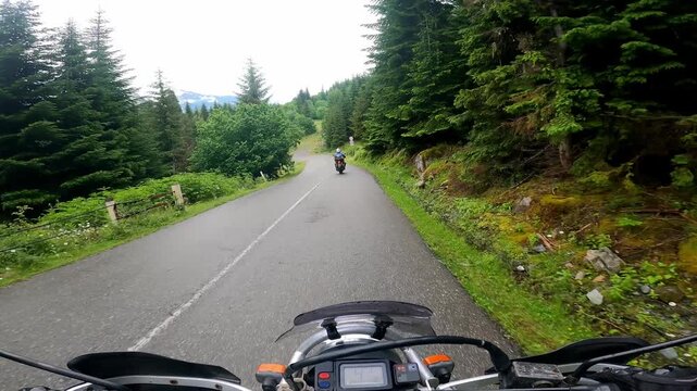POV motorcycle ride through dense fog on a winding mountain road in Svaneti, Georgia. Scenic forest highway with another rider ahead, creating an atmospheric adventure travel experience