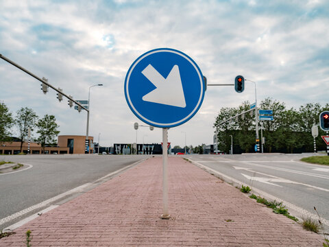 A blue mandatory-direction traffic sign with an arrow stands beside a cycle path at a junction.