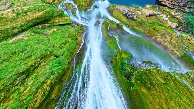 Moss-covered waterfall flowing over layered limestone rock in a lush landscape, offering a refreshing travel, tourism, and environmental background.