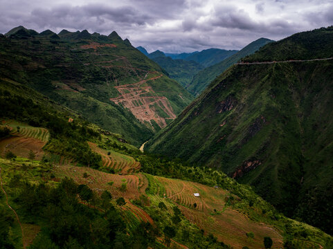 Aerial view of the mountainous landscape near the northernmost point of Vietnam at the Chinese border, featuring terraced fields, winding roads, and lush green hills in Lung Cu, Tuyen Quang, Vietnam.