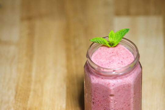 Fresh strawberry smoothie in glass jar with mint on wooden background