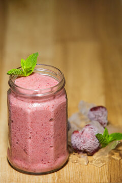 Fresh strawberry smoothie in glass jar with mint on wooden table