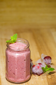 Fresh strawberry smoothie in glass jar with ice mint on wooden background