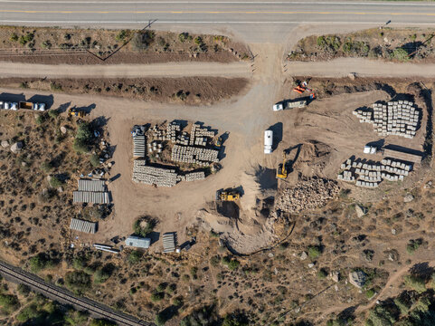 Aerial view of a construction site with piles of concrete blocks, heavy machinery, and a truck parked on a dirt lot near U.S. Highway 6 and railroad tracks in Wolcott, Colorado, United States.