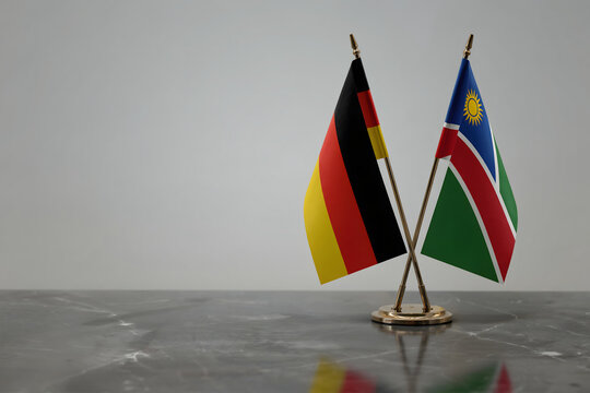 Miniature flags of germany and rwanda standing on a dark marble table in a blurred office setting with soft lighting and neutral background