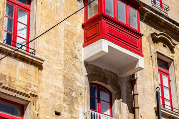 Vivid red wooden gallarija balcony contrasts with weathered limestone facade and matching red-shuttered windows in Valletta, Malta © Tony Blood