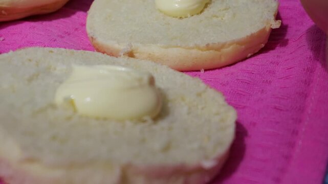 Freshly sliced burger buns rest on a bright pink cloth surface with a dollop of creamy mayonnaise. The soft baked bread serves as a base for preparing homemade burgers and quick snacks.