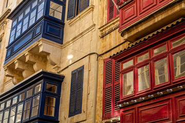 Contrasting navy and red gallarija balconies with open wooden shutters line a limestone facade in Valletta, Malta © Tony Blood