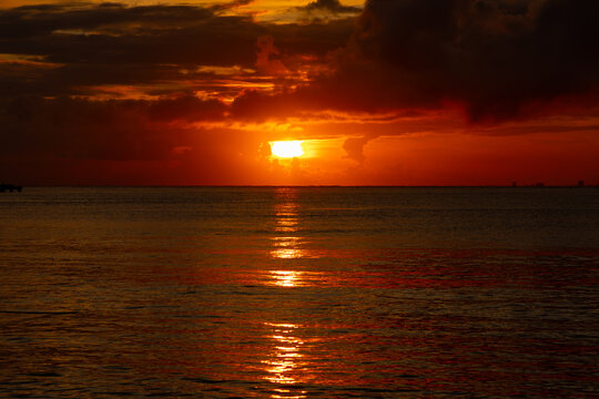Vivid sun breaking through dark clouds over the ocean horizon with brilliant reflection.