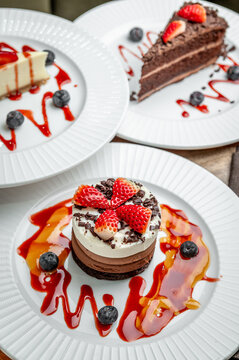 Desserts served on white plates at cafe. Three desserts are displayed on white plates at a cafe. Each dessert has toppings and sauces.