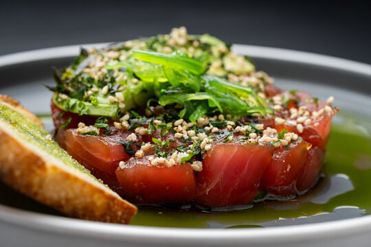 Herbed fish with veggies. A plate shows diced fish topped with herbs and vegetables, garnished with sesame seeds, served on a light sauce.