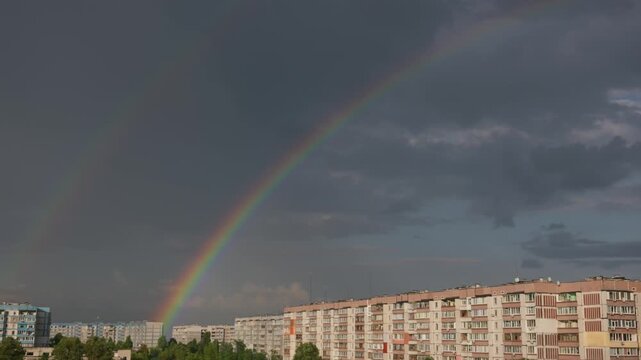 A bright full rainbow arches over Soviet-style apartment buildings after a thunderstorm. Dark rain clouds fill the sky, contrasting with the colorful spectrum and signaling urban optimism.