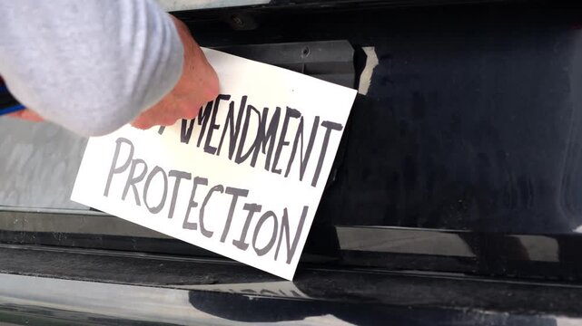 Man attaching protest license plates to vehicle using screwdriver, illustrating citizen pushback against ALPR surveillance - Fourth Amendment privacy