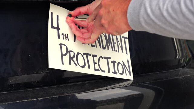 Man attaching protest license plates to vehicle using screwdriver, illustrating citizen pushback against ALPR surveillance - Fourth Amendment privacy