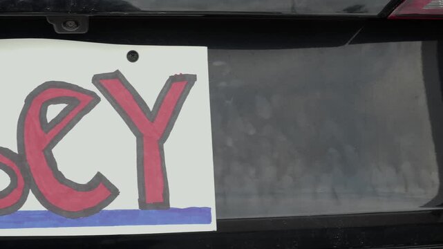 Man attaching protest license plates to vehicle using screwdriver, illustrating citizen pushback against ALPR surveillance - Fourth Amendment privacy