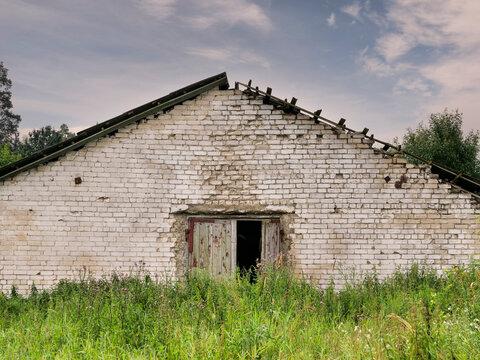 Old worn out farm or warehouse building with damaged roof and white brick walls. Rising supply price and troubled economy effect on running a ranch. Abandoned farm. Sad and shocking mood and feel.