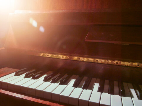 Piano keys under warm, soft lighting. Shallow depth of field highlights keyboard texture. Wooden casing partially visible in background. Focus on black and white keys with gentle blur. Sun flare.