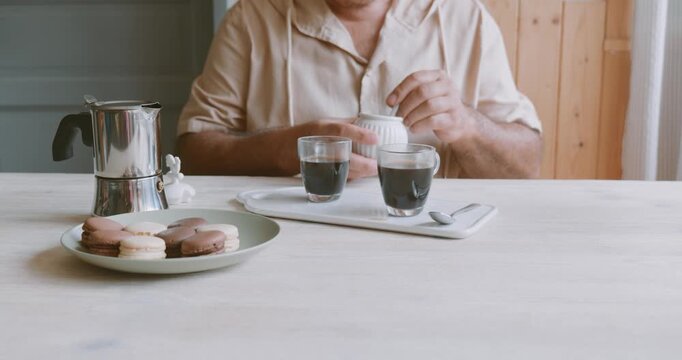 Man making coffee at home, putting cane sugar into glass coffee cup with hot coffee. Preparation home coffee, morning ritual, coffee brewing process.