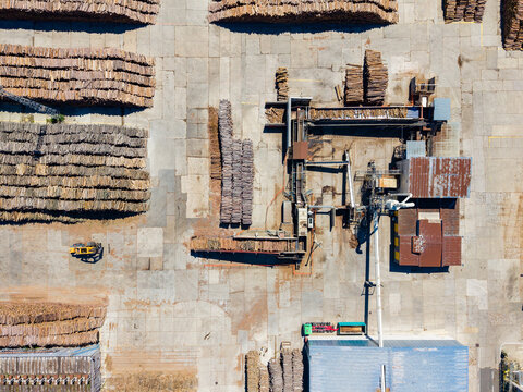 View of a lumber yard with stacks of logs and machinery for processing at a timber mill during the day
