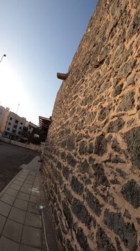 Walking along the traditional stone wall exterior of historic masjid shikhan.