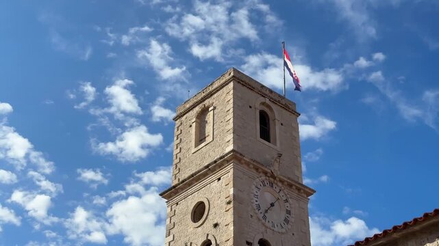Old stone clock tower with the flag of Croatia waving in the wind against a blue sky with clouds